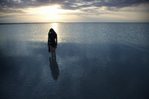 a woman standing in the ocean at sunset 