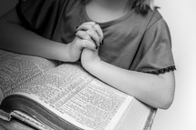 Girl's praying hands resting on an open Bible.