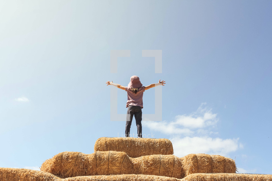 little girl standing on hay bales 