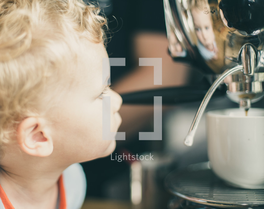 child looking at his reflection in a coffee maker 