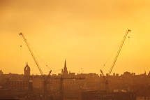 construction cranes in a city under an orange sky 