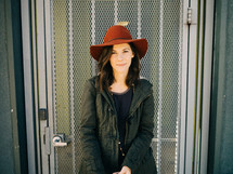 A woman in a red hat stands in front of a metal grid door.
