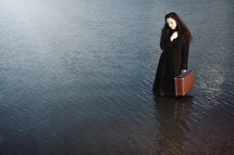 a woman holding a suitcase standing in water 