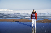 a woman in a snowsuit standing outdoors in wet sand 