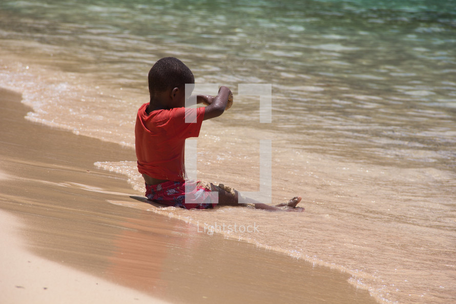 a child sitting on a beach letting the tide roll over his legs 