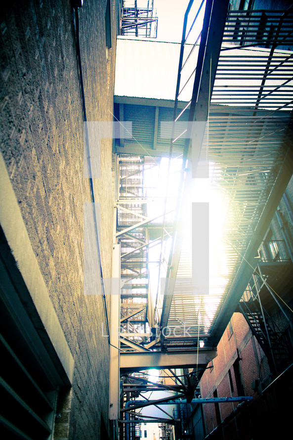 fire escape on an old apartment building  with a sun flare coming out of the sky. 