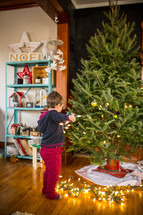 a boy putting Christmas lights on a Christmas tree 