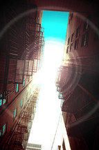 Sunlight between fire escapes of two apartment buildings.