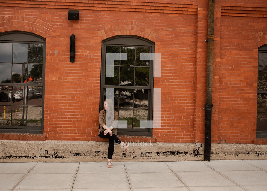 woman sitting near a red brick warehouse building 