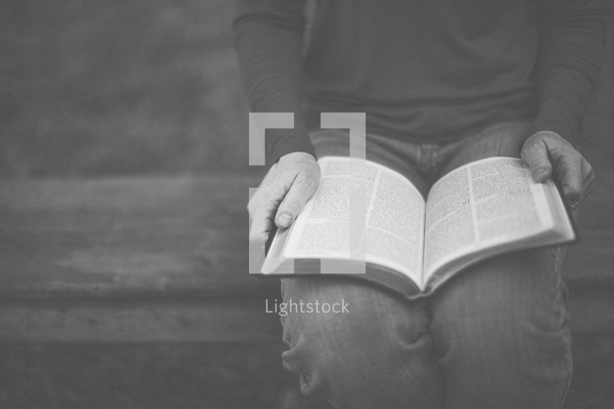 A woman sitting on a bench and reading the Bible