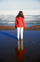 a woman in a snowsuit standing outdoors on wet sand 