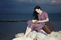 a woman sitting on a rock by the ocean reading a Book 