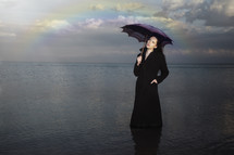 a woman holding an umbrella standing in water under a rainbow 