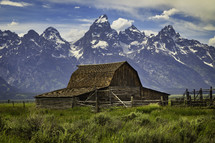 A daytime view of the Mormon Row barn below the Grand Teton Mountain Range on a cloudy day