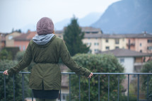 woman standing at a railing looking out at the view of a European town 