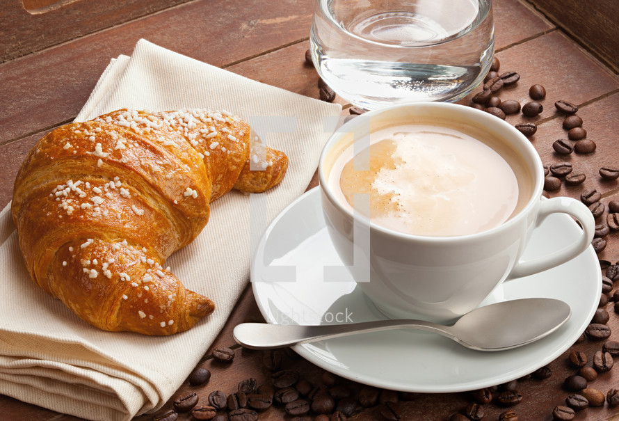 Cappuccino with croissant and glass of water in the tray of brown wood