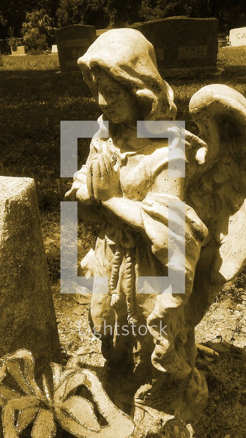 A Sepia tone image of a praying angel statue at a grave site in a local cemetery.  