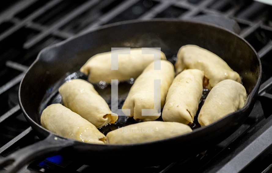 Frying egg rolls in a pan on a gas stove