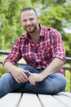 a man in a plaid shirt sitting outdoors 
