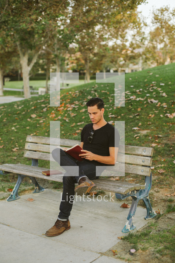 man sitting on a park bench reading a Bible 