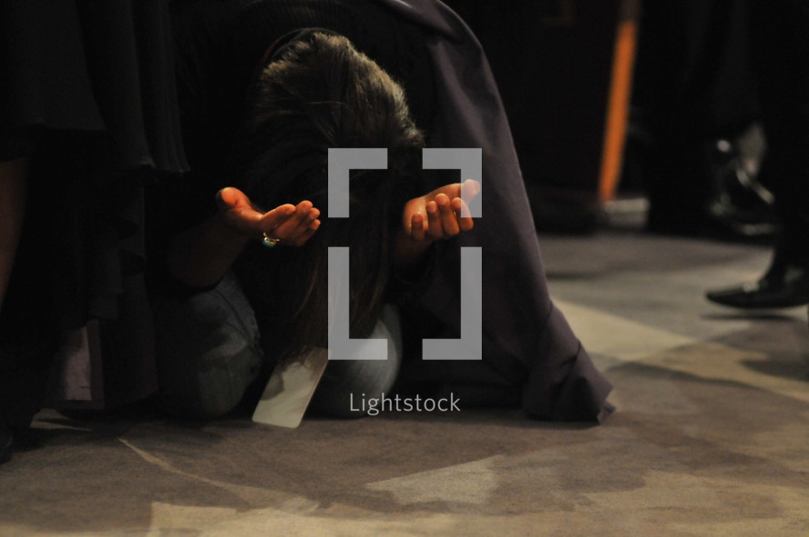 Woman kneeling with arms extended, praising God during worship service.