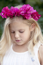 Girl in white dress with pink flowers in her hair looking down in prayer.