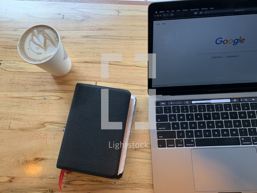 laptop computer, Bible, and coffee cup on a wood table 