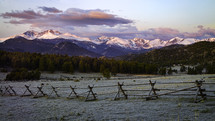 rustic fence in a field and snow capped mountains 
