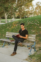 man sitting on a park bench reading a Bible 