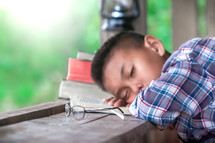 a boy sleeping on an open Bible outdoors 