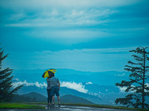 couple under an umbrella looking out at a mountain view 