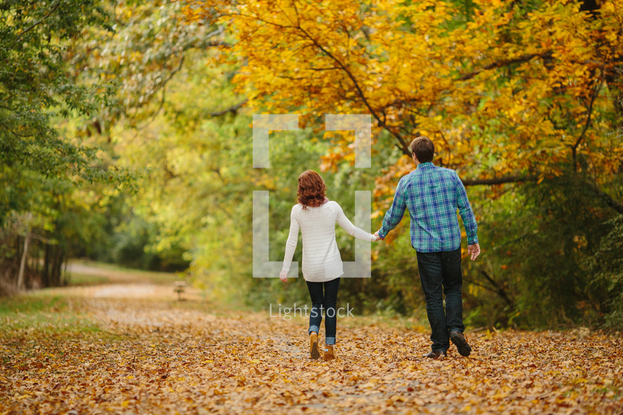 couple walking holding hands through fall leaves 