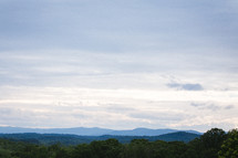 Treetops and mountains on the horizon under a cloudy sky.