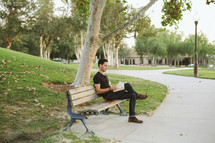 a man reading a Bible while sitting on a park bench 