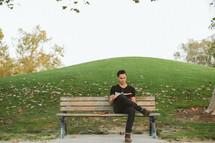 man reading a Bible while sitting on a park bench 