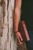 man leaning against a tree holding Bible 