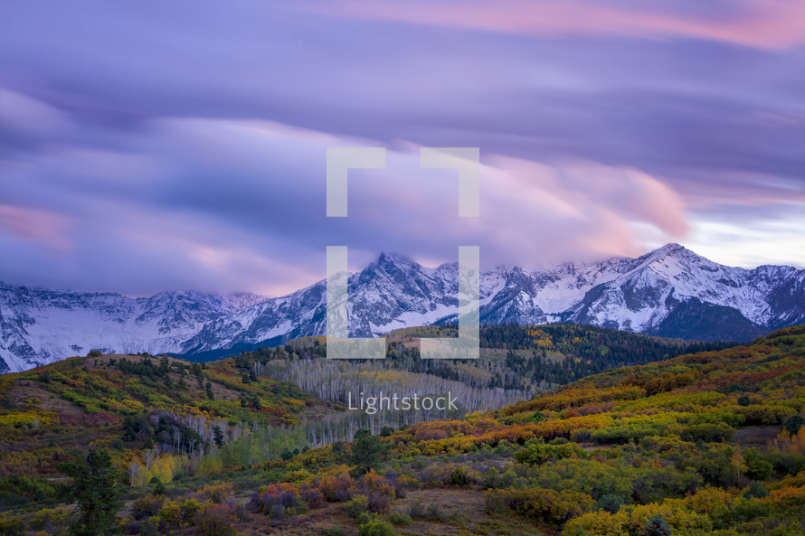colorful autumn mountain forest and snow capped mountain peaks at sunset 
