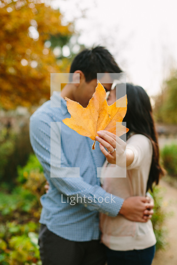 man and woman kissing behind a leaf 