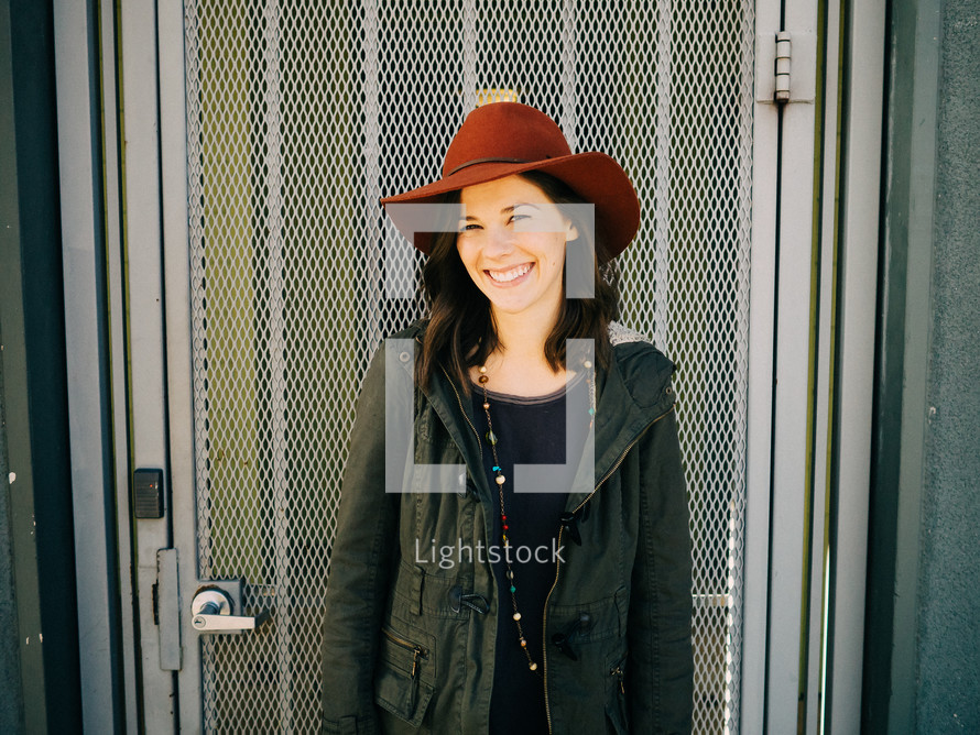 A smiling young woman in a red hat stands in front of a metal grid door.