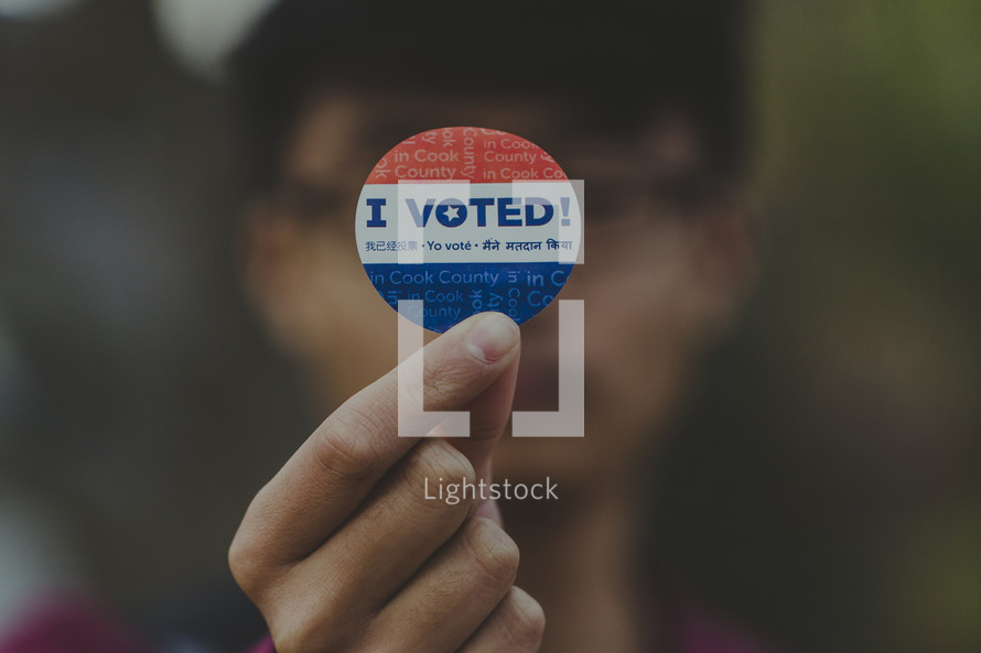 man holding up an I voted sticker 