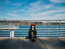 A woman in a red hat leans against a railing by a lake.