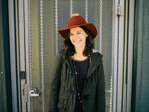 A smiling young woman in a red hat stands in front of a metal grid door.