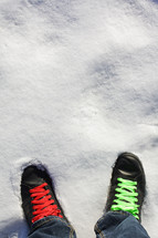 green and red shoe laces on a pair of black shoes standing in the snow