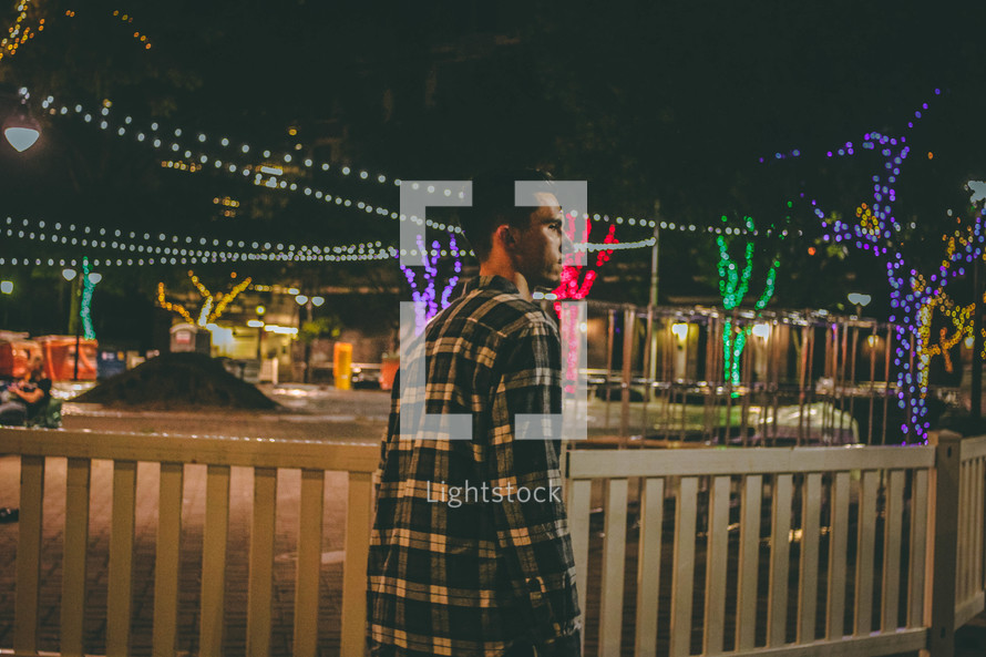 man walking outdoors at night and a Christmas lights display 