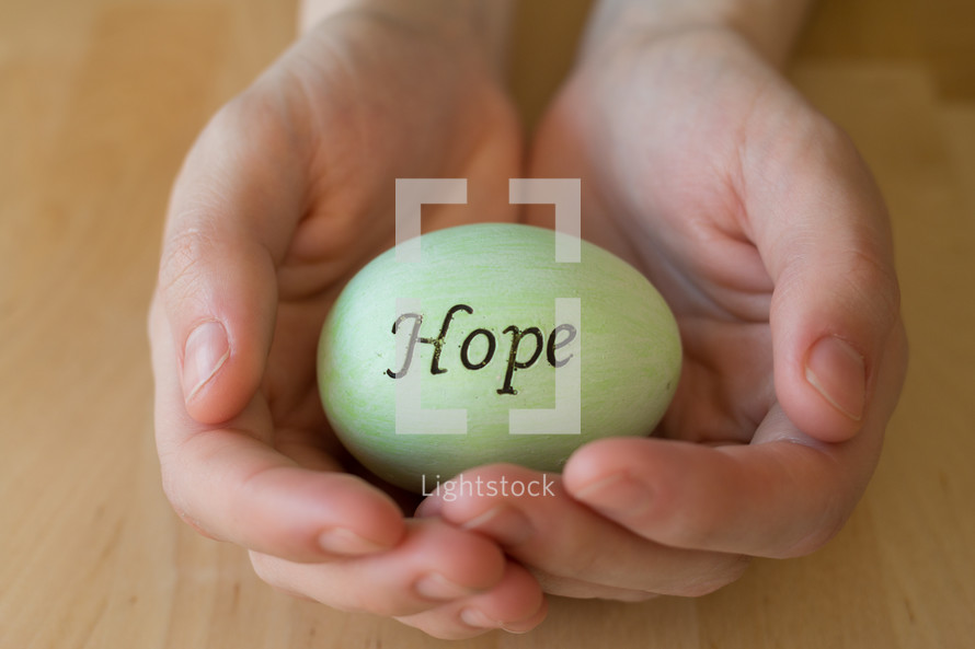 Hands cradling a green egg reading, "hope."