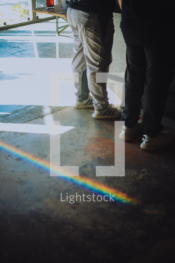 rainbow reflecting on concrete behind two people standing 