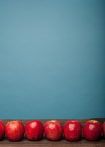 A row of red apples on a wooden surface with a blue background.