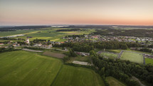 Aerial view of the small town Fjärås, Kungsbacka, in Sweden. Beautiful and lush farmlands with forest surrounding them while the sun sets and warms the atmosphere.