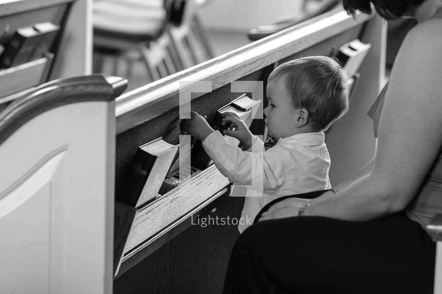 toddler boy playing with hymnals in the back of a pew in a church 