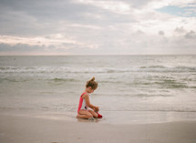 child in a bathing suit playing in sand on a beach 